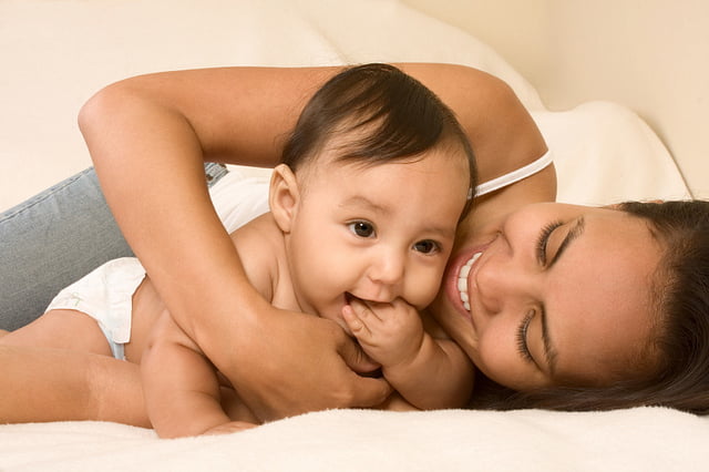 Mother playing with her baby boy son on bed