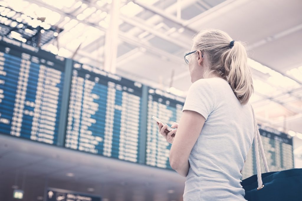 A woman holding a phone in an airport. <a href="http://dep.ph/v/zj761t-bsat0" target="_blank">Deposit Photos</a>