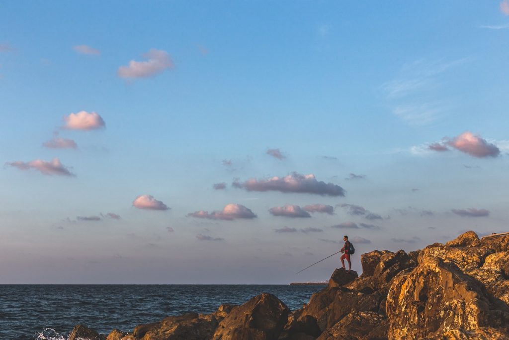 A man fishing with a fishing rod on the breakwater near Tel Aviv. Deposit Photos