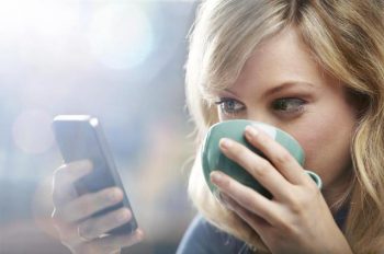 woman smiling drinking coffee looking at phone via BigStock