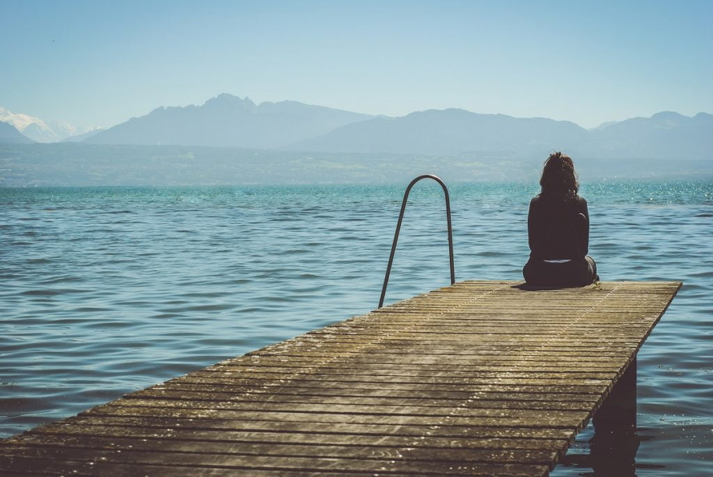 A woman sitting by a lake. Photo by Paola Chaaya on Unsplash