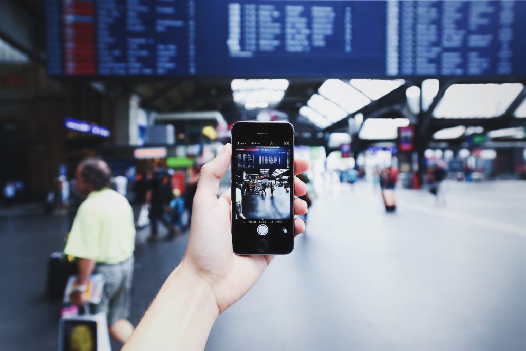 A person using a phone at a train station. Photo via Pexels