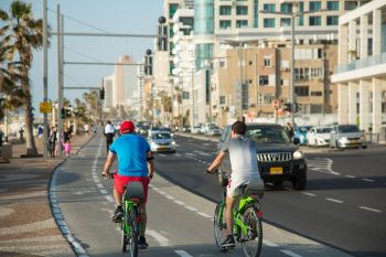 People riding bikes on a bike pass of a seaside promenade in Tel Aviv. Deposit Photos