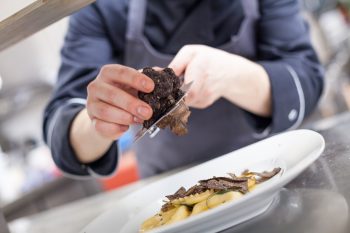 An illusrtrative photo of a chef grating truffle mushroom shavings onto homemade ravioli.